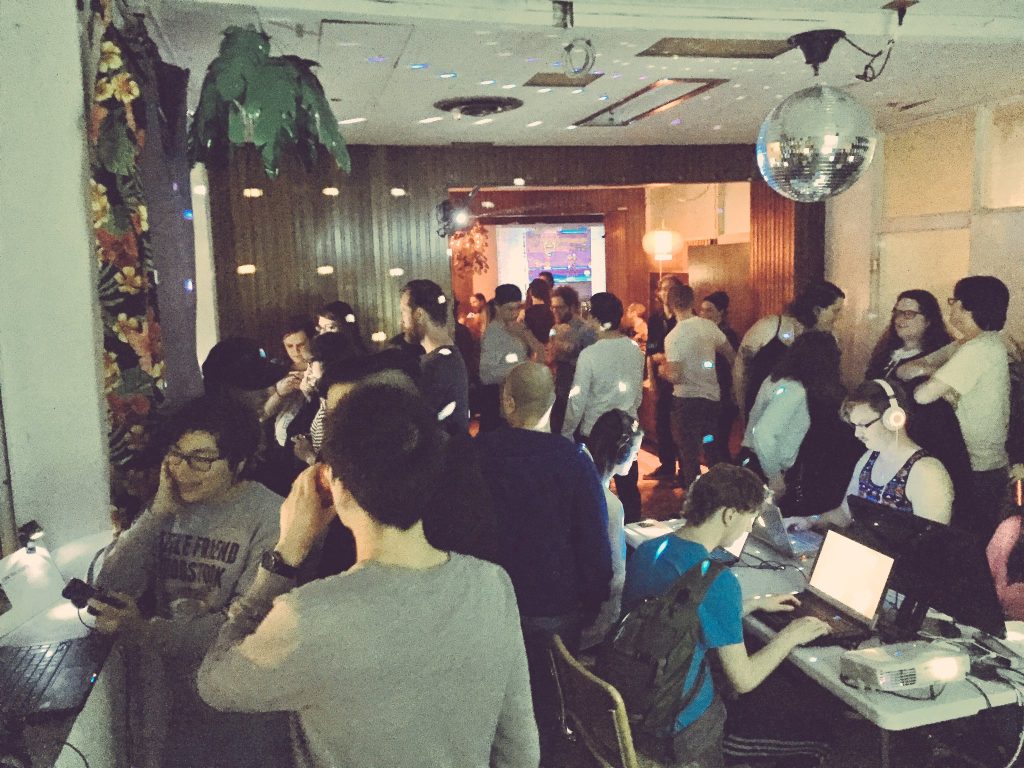 An image of a meet-up with multiple game developers. There are disco lights and multiple people on laptops.